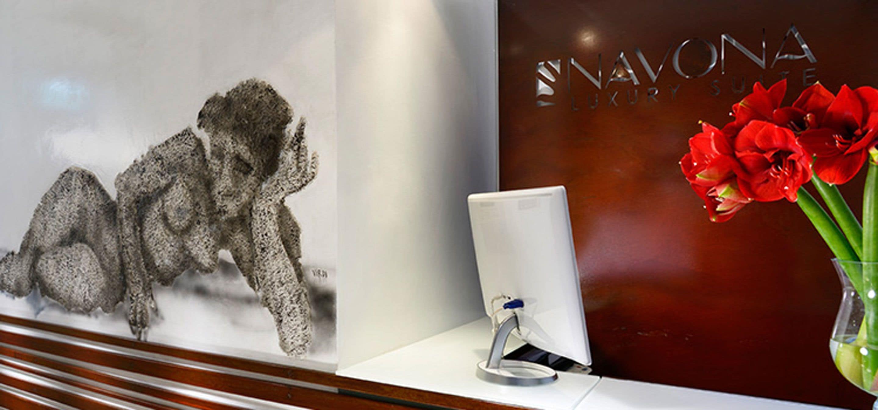 A reception desk with a framed artwork, a white desk lamp, and a vase with red flowers.