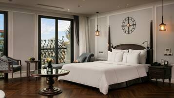 A hotel room with a large bed, a round table, a chair, a nightstand, and a balcony with a railing.