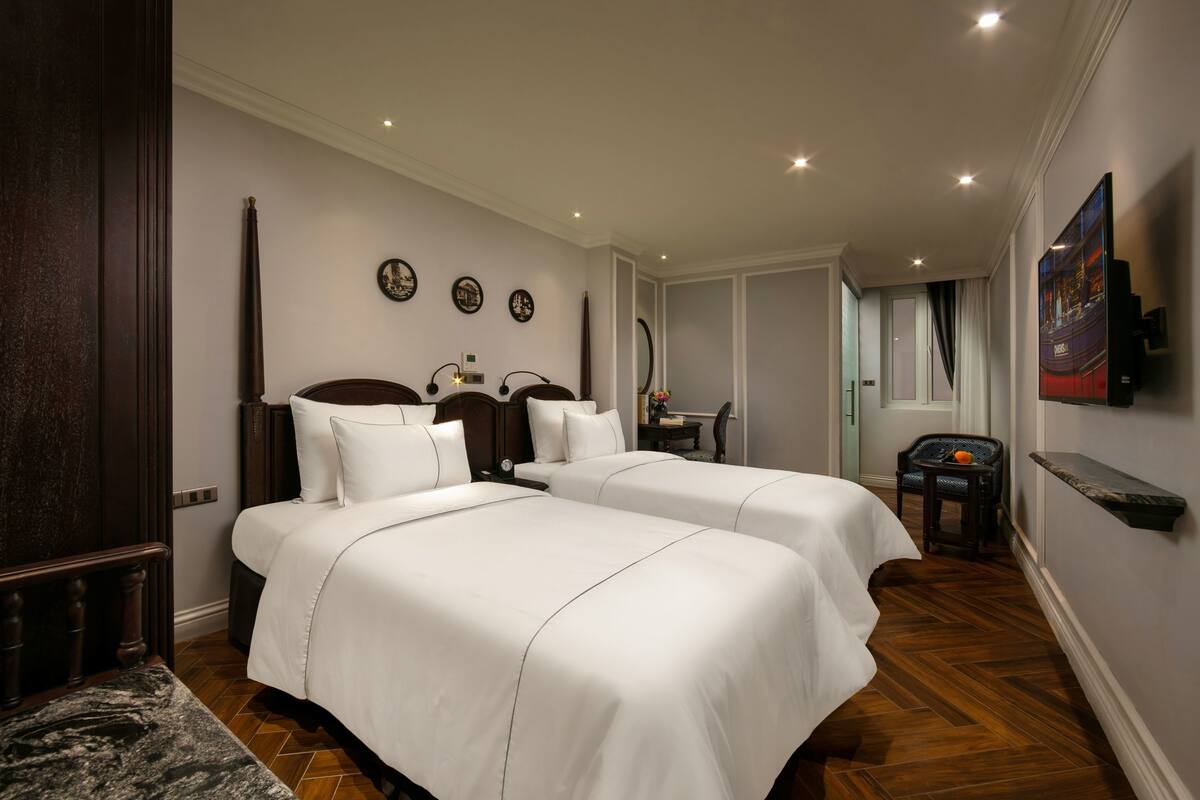 A hotel room with two beds, a wooden headboard, a small table, and a chair.