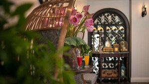 Une chaise en osier, un vase rempli de fleurs roses et deux verres de jus d’orange.
