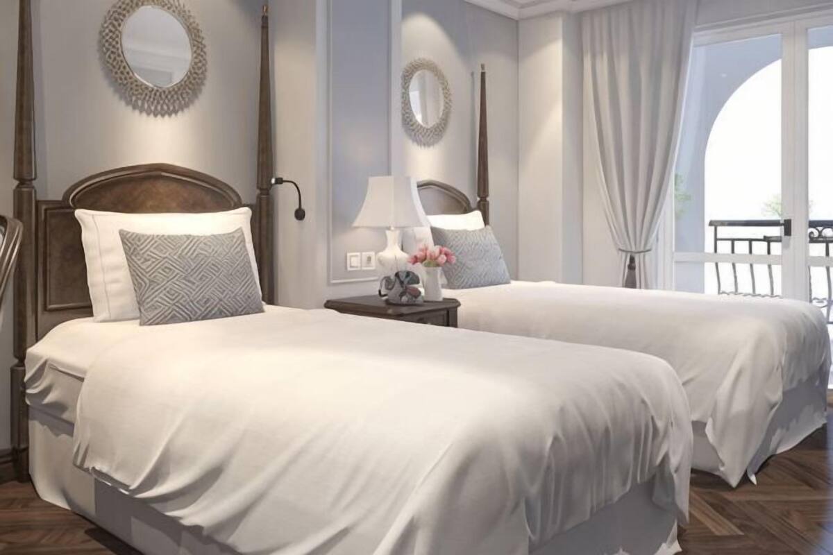 A hotel room with two beds, a nightstand, a lamp, and a view of the outdoors.