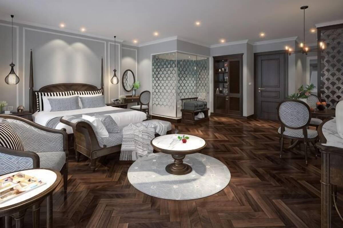 A modern hotel room with a large bed, a sitting area with a round table, and a separate dining area.