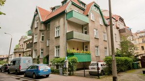 A multi-story building with a green balcony, parked cars, and a van with 'DCC' on it. - Imperial Apartments - Winieckiego (Sopot)