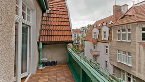 A balcony with a wooden floor, a green railing, and a view of neighboring buildings with red-tiled roofs. - Imperial Apartments - Winieckiego (Sopot)