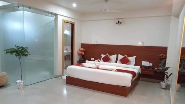 A modern hotel room with a large bed, a glass door leading to a bathroom, and a small bedside table with a vase of flowers. - Hotel Royal Amer City (Amer)