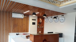 A hotel reception desk with a wooden finish, a reception area, and three wall clocks. - Hotel Royal Amer City (Amer)