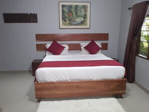 A bed with a wooden frame, white bedding, and two red pillows. There is a painting on the wall above the bed.