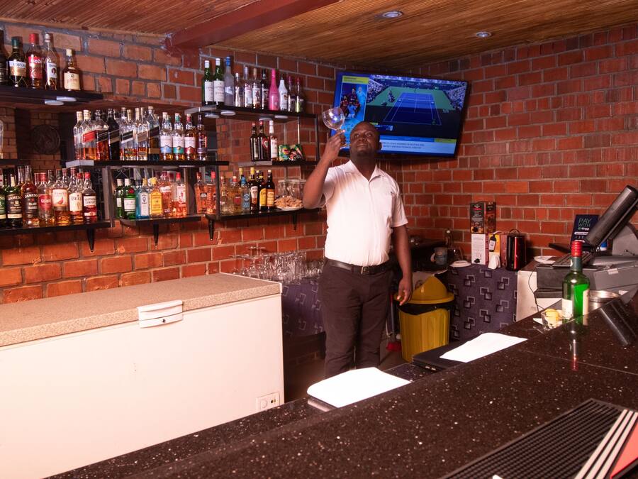 Een bar met drankflessen op de planken, een televisiescherm en een toonbank met kassa.