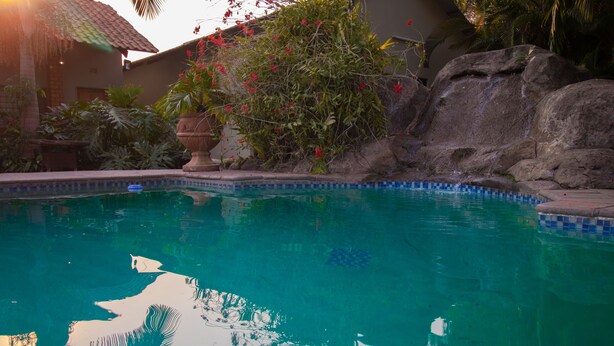 A clear swimming pool with a tiled edge, surrounded by rocks and plants. - Sherbourne Lodge (Kitwe)