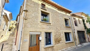 A two-story stone building with a wooden door and windows, a small balcony with plants, and a sign indicating it is a home. - Home 12 "les Vignes" (Châteauneuf-du-Pape)