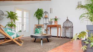 A cozy living room with a wooden chair, a round table, and various potted plants. - Home 12 "les Vignes" (Châteauneuf-du-Pape)