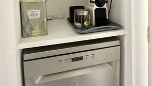 A kitchen with a microwave on the upper shelf, a canister labeled "Fashion Living Green Forest" on the middle shelf, and a coffee maker on the lower shelf. - Home 12 "les Vignes" (Châteauneuf-du-Pape)