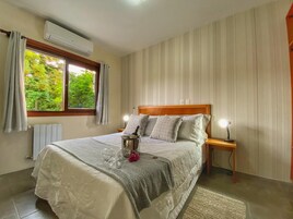 Quarto bem arrumado com cama, mesa de cabeceira e janela com cortinas.