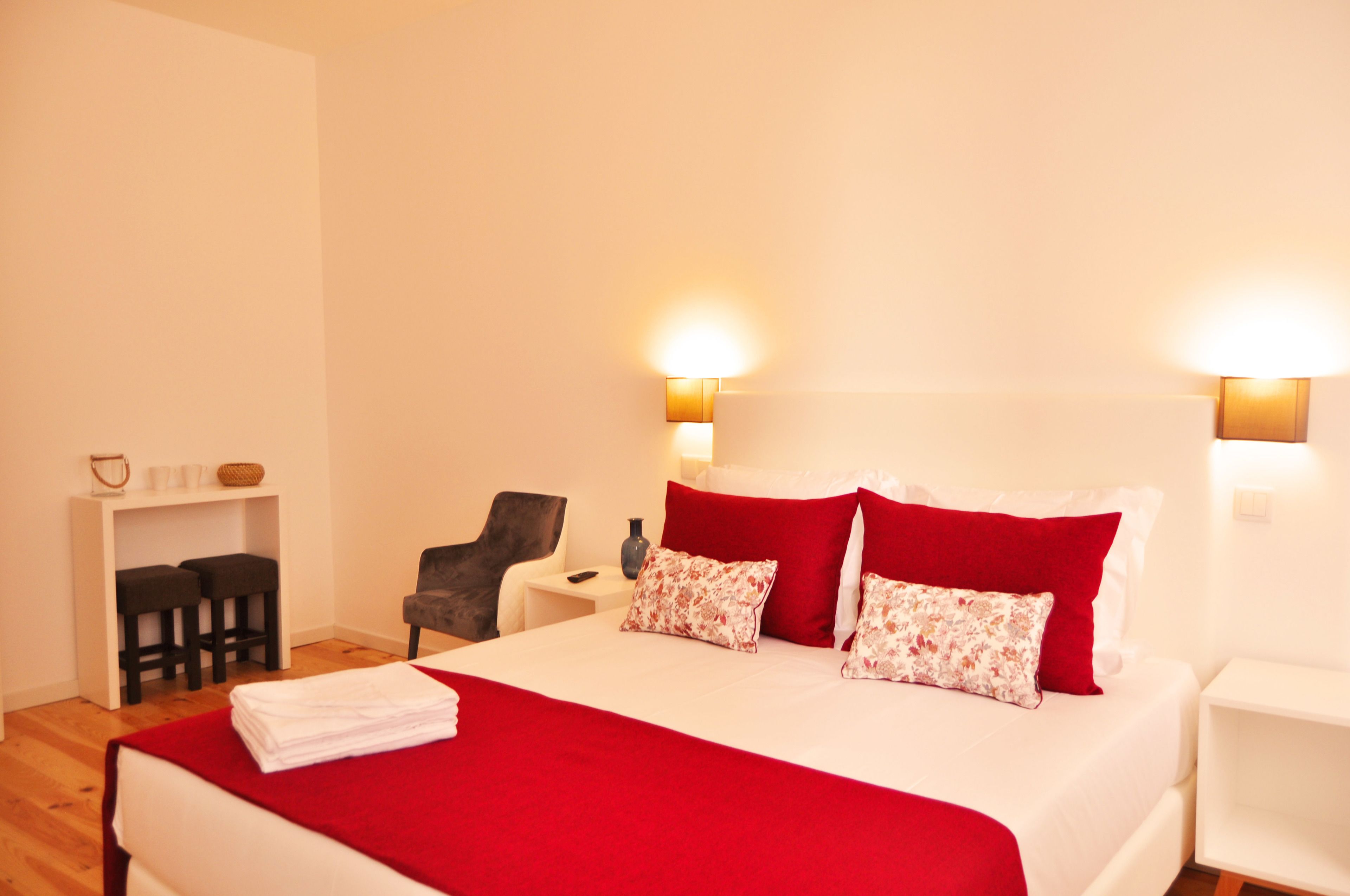 A hotel room with a bed, a desk with two chairs, a small table, and two wall-mounted lamps.