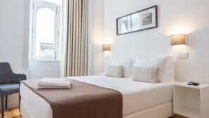 Una habitación de hotel moderna con una cama grande, mesitas de noche, una silla y un ventanal con cortinas.