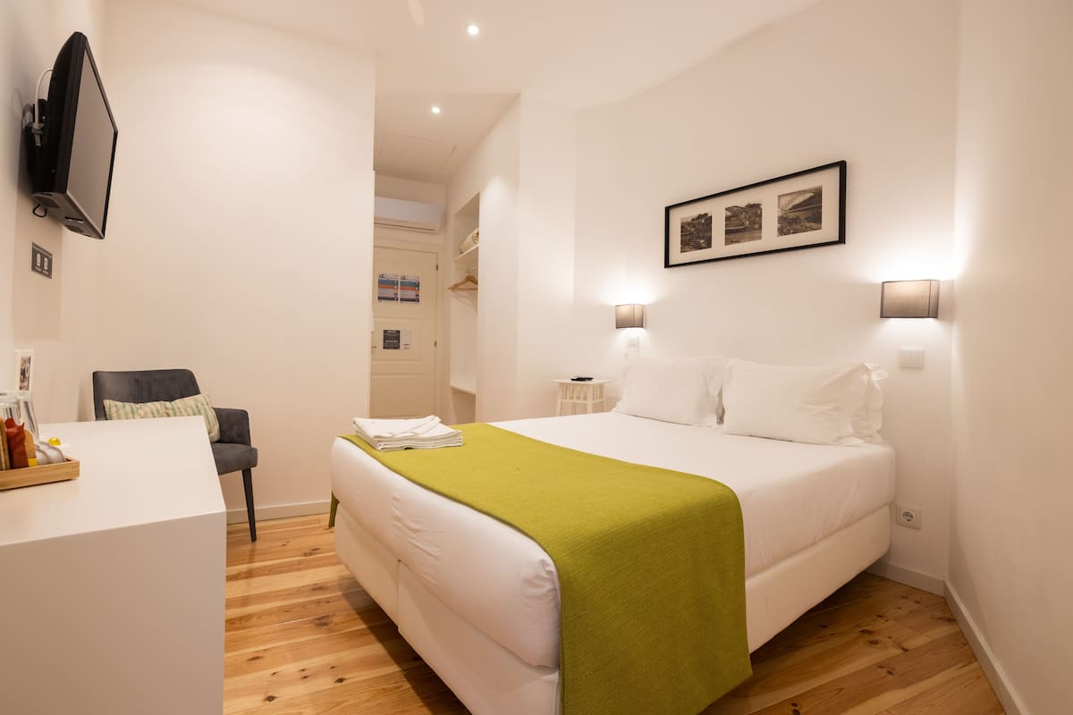A hotel room with a bed, a desk, a chair, and a TV mounted on the wall.