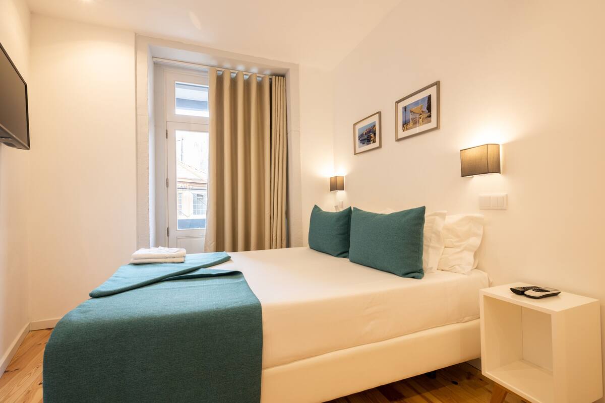 A modern hotel room with a large bed, a bedside table, and a window with curtains.
