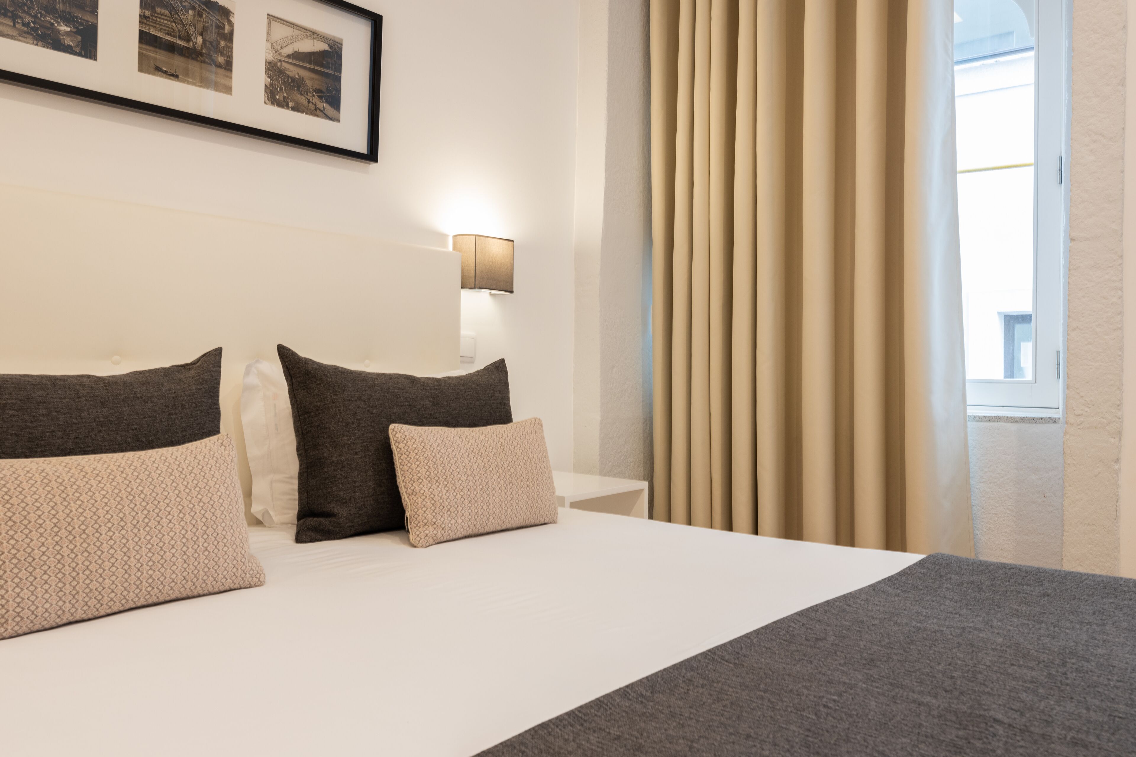 Una habitación de hotel con una cama grande, una mesita de noche con lámpara y un ventanal con cortinas.