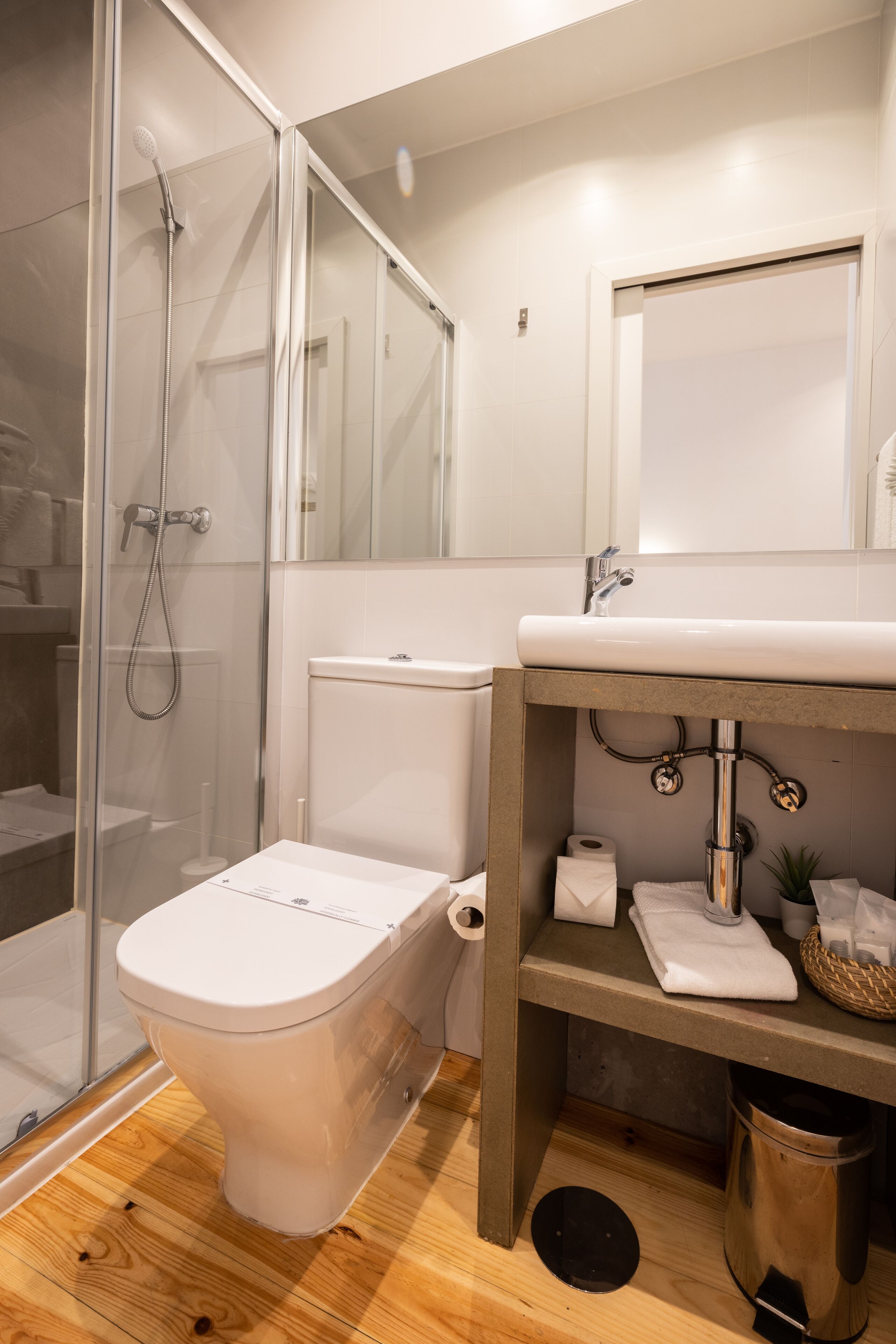 Een moderne badkamer met een douchecabine van glas, een wit toilet en een houten wastafelmeubel met een wastafel.