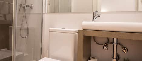 A modern bathroom with a glass shower enclosure, a white toilet, and a wooden vanity with a sink.