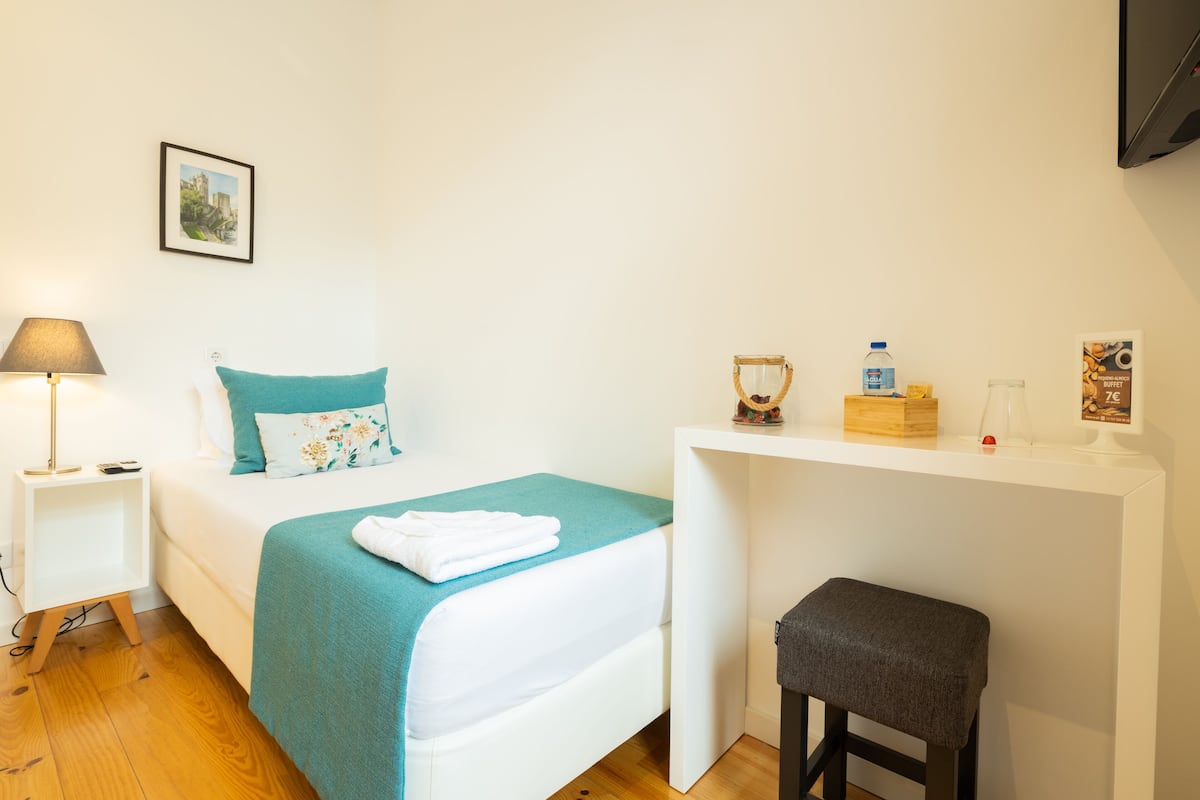 A neatly arranged bedroom with a bed, bedside table, and a small stool.