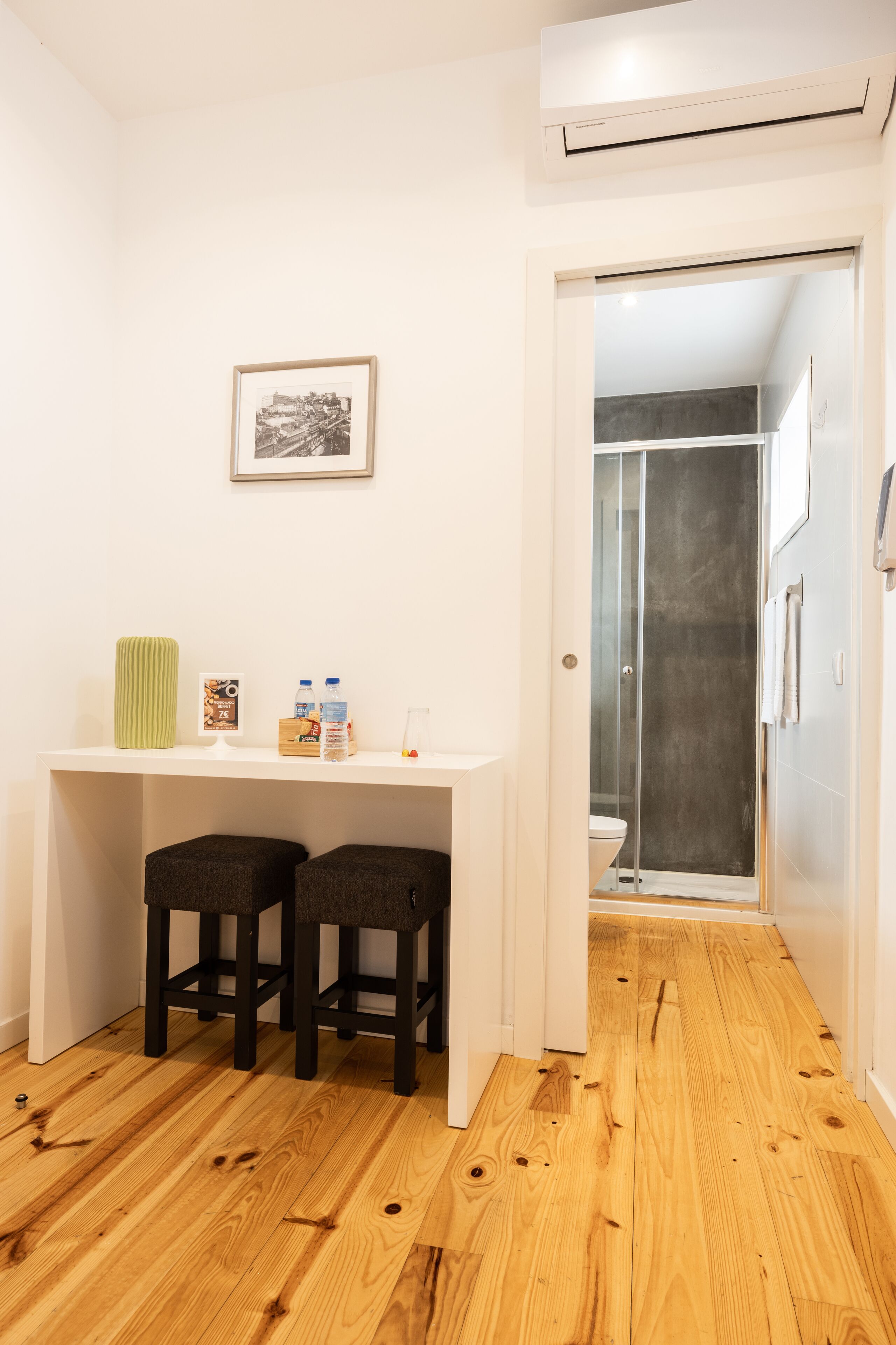 A bathroom with a shower, a toilet, and a small desk with stools.