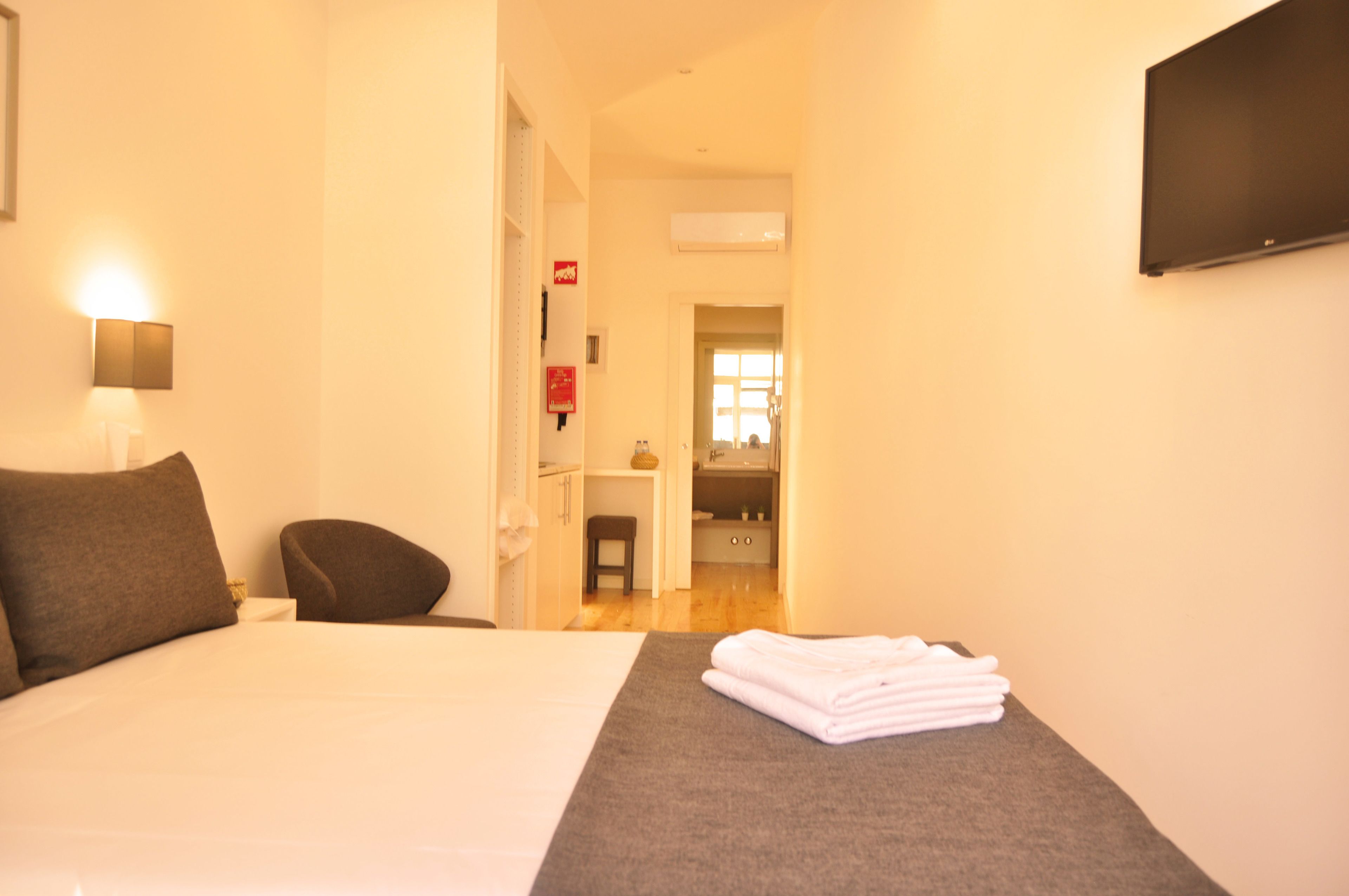 Una camera d'albergo con un letto, una sedia, una TV e un bagno sullo sfondo.