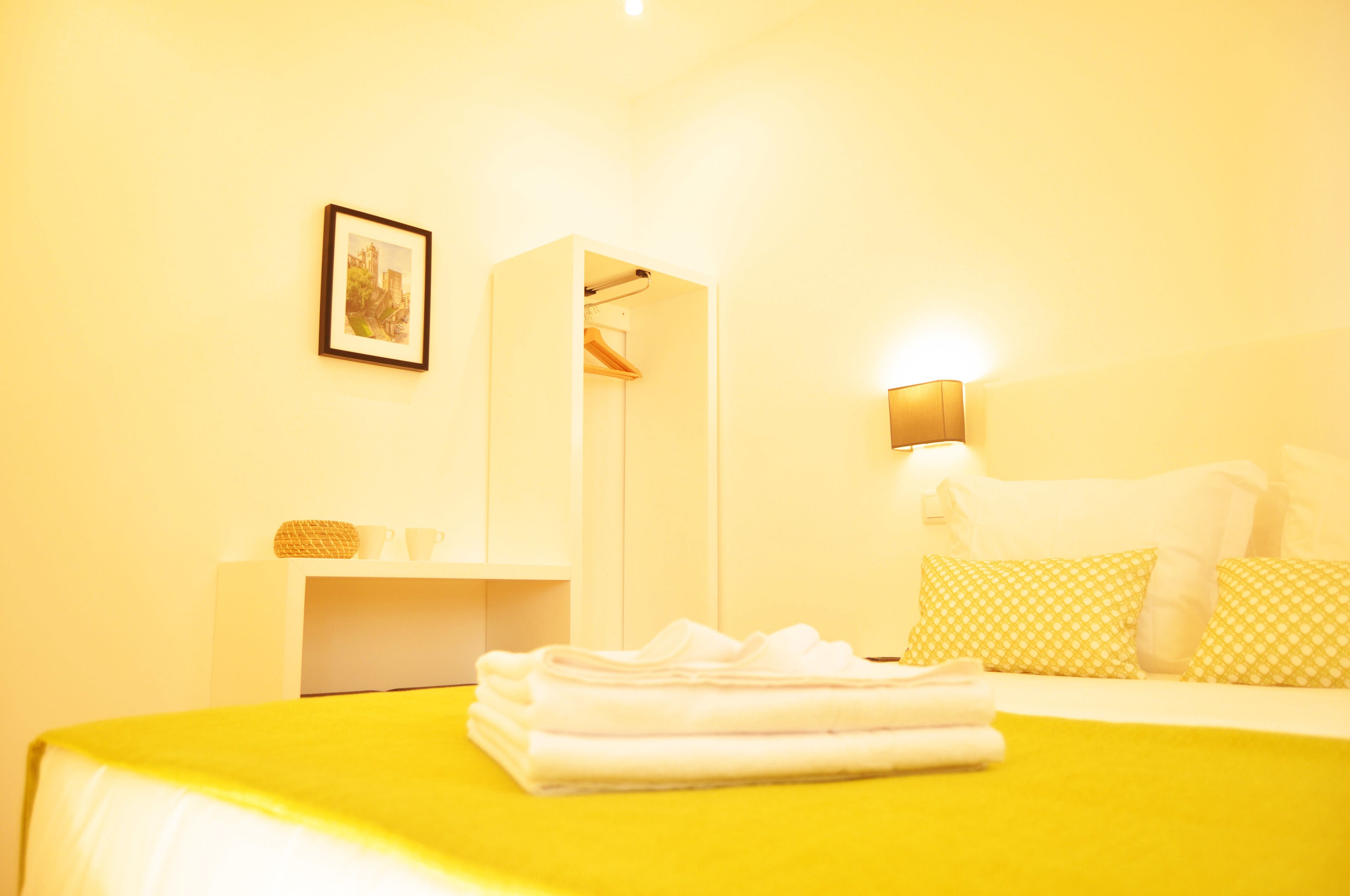 Ein Hotelzimmer mit einem Bett, einem Nachttisch, einem Kleiderhaken und einer Wandleuchte.