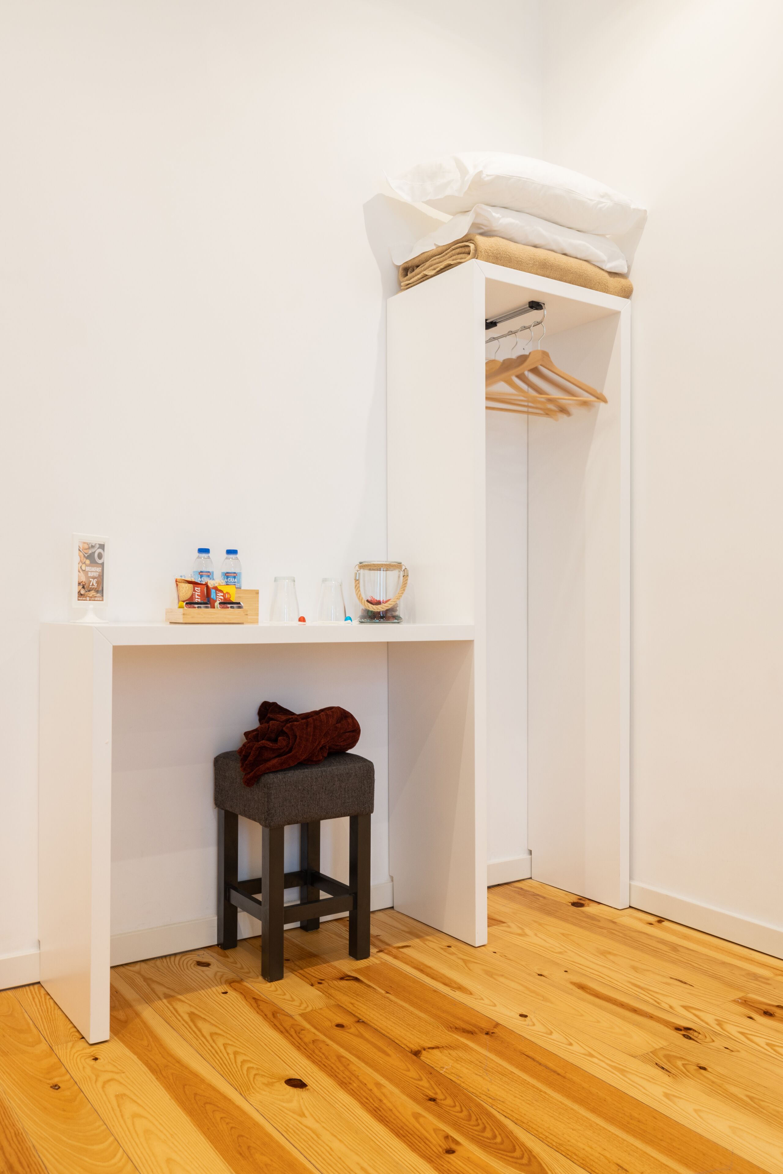 Une petite pièce blanche avec un plancher en bois, un bureau avec une chaise et un porte-manteau mural.