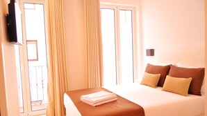 Una habitación de hotel con cama, cortinas, televisor y balcón.