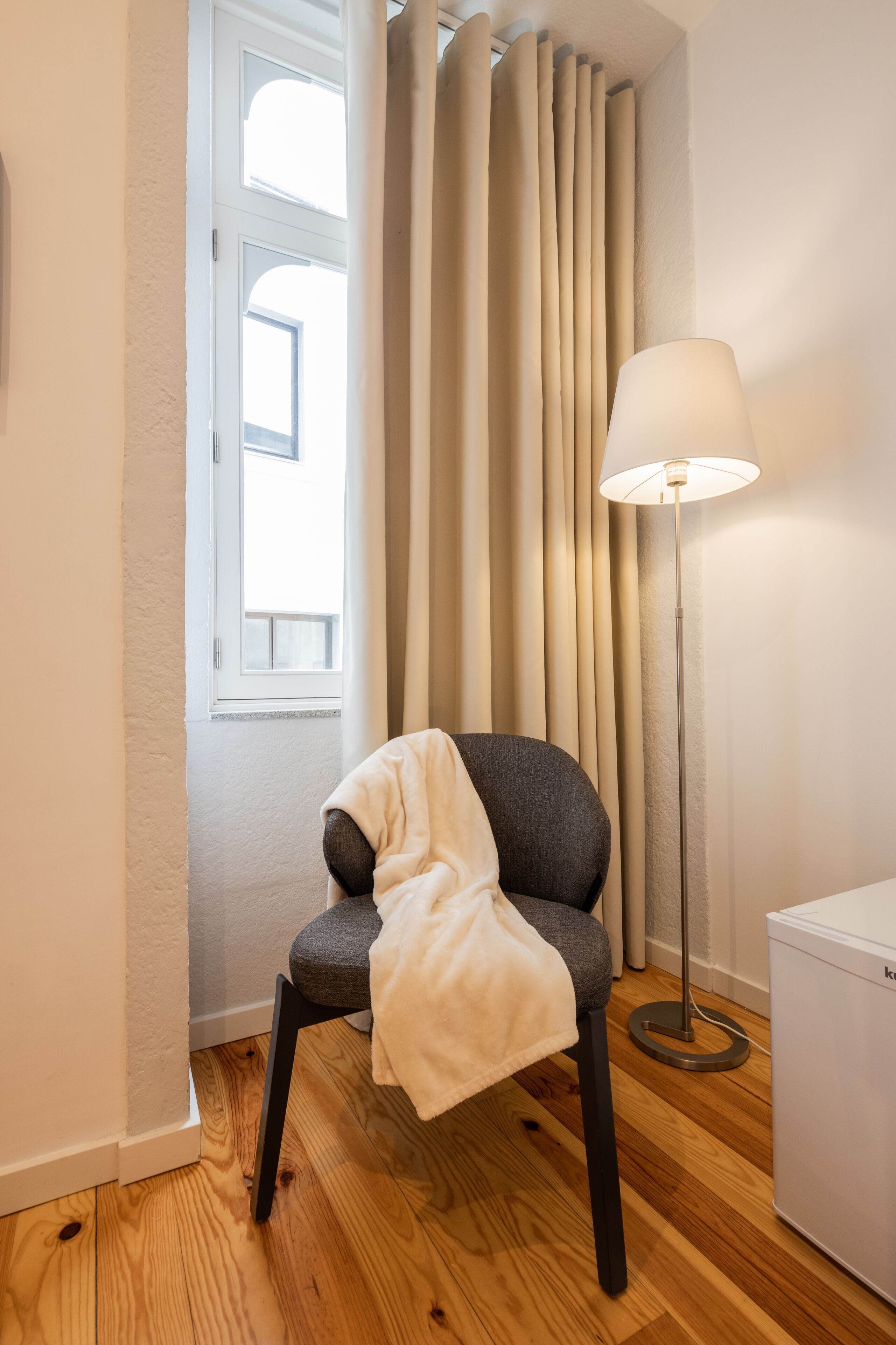 A room with a chair, a floor lamp, and a window with curtains.