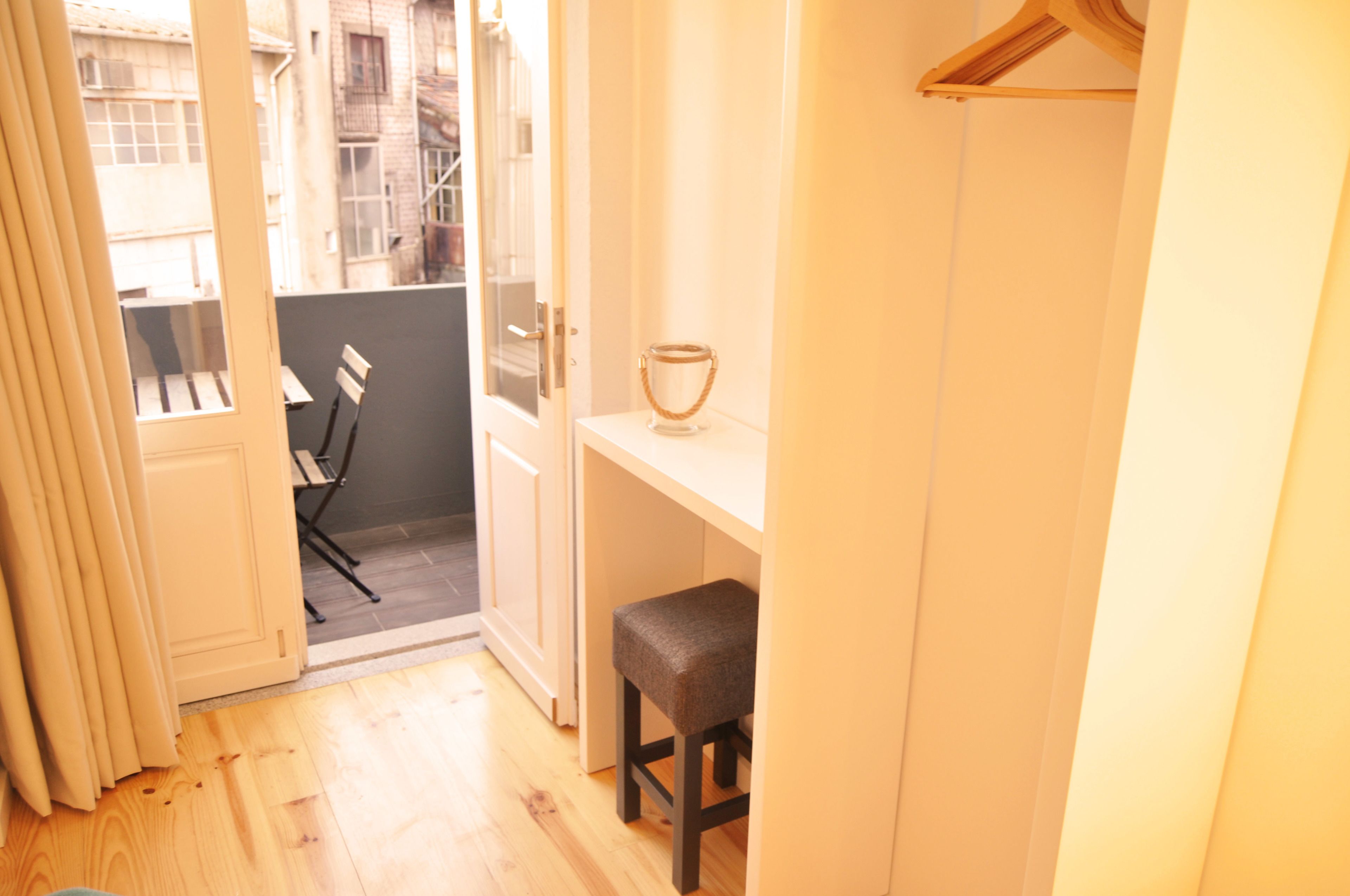 A small, bright room with a wooden floor, a white desk, a chair, and a hanging coat rack.
