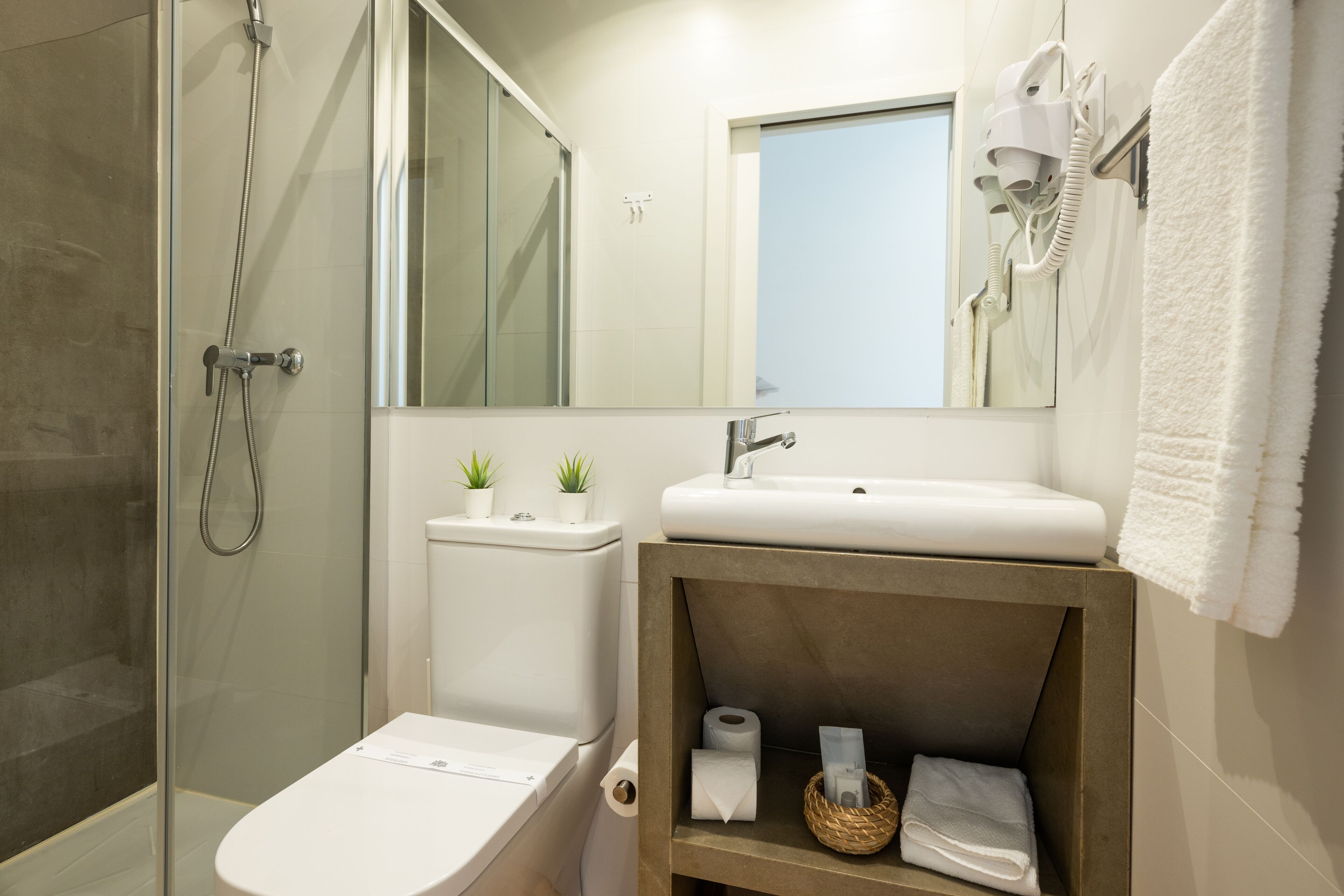 A modern bathroom with a glass-enclosed shower, a white sink, and a mirror above it. There is a towel rack with a white towel hanging on it.