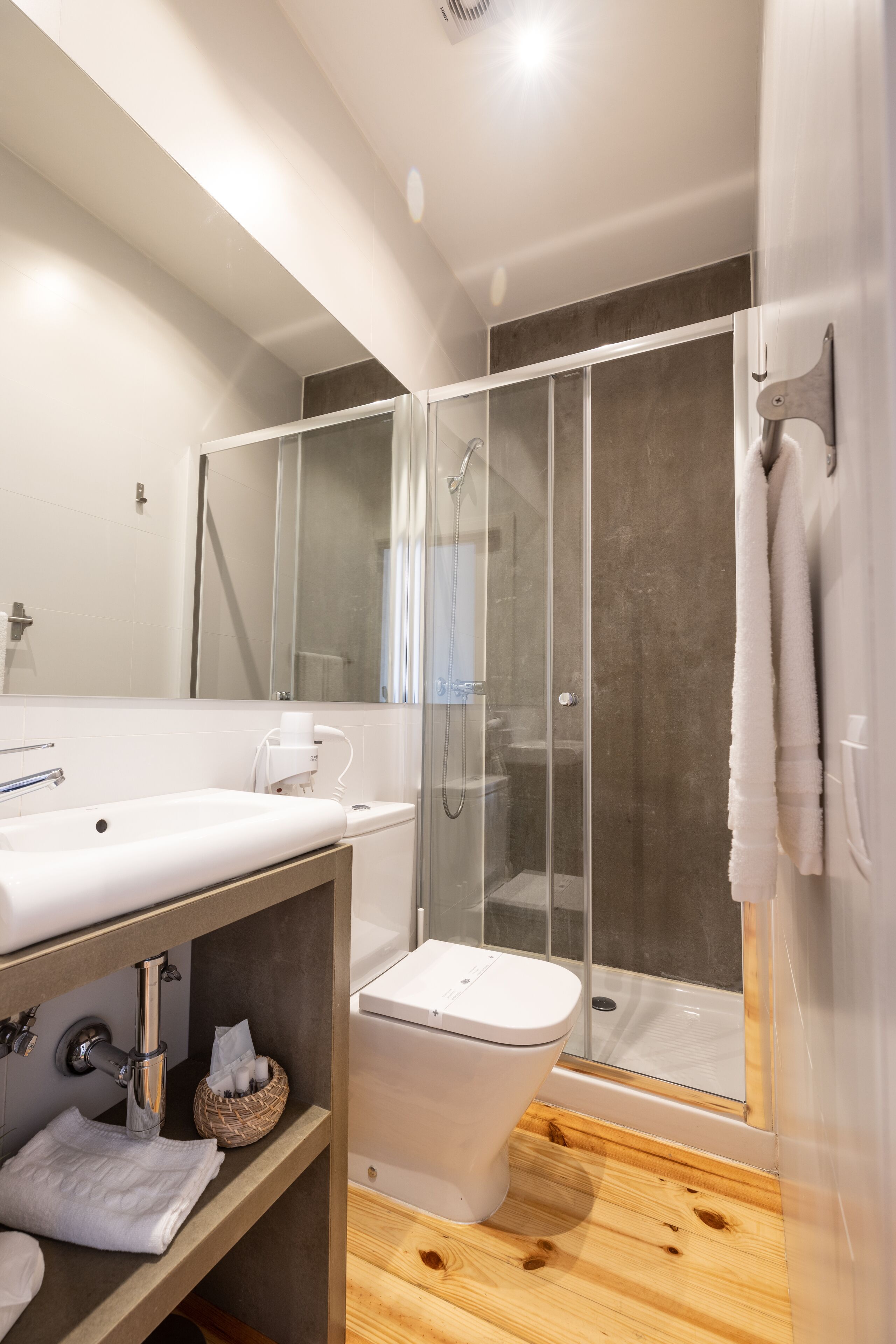 A modern bathroom with a glass shower enclosure, a white sink, and a wooden vanity.