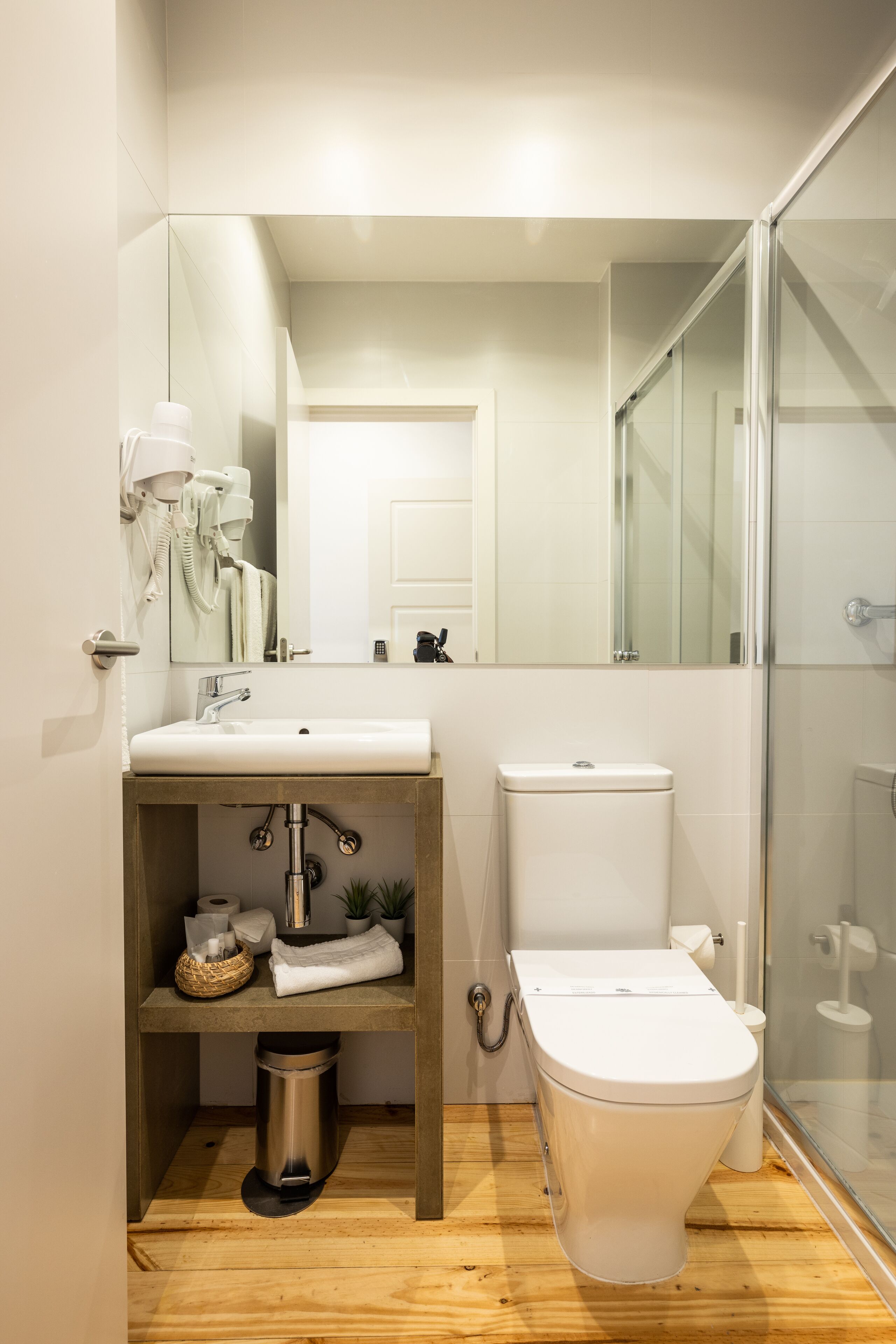Une salle de bain moderne avec un meuble-lavabo en bois, des accessoires blancs et une cabine de douche en verre.