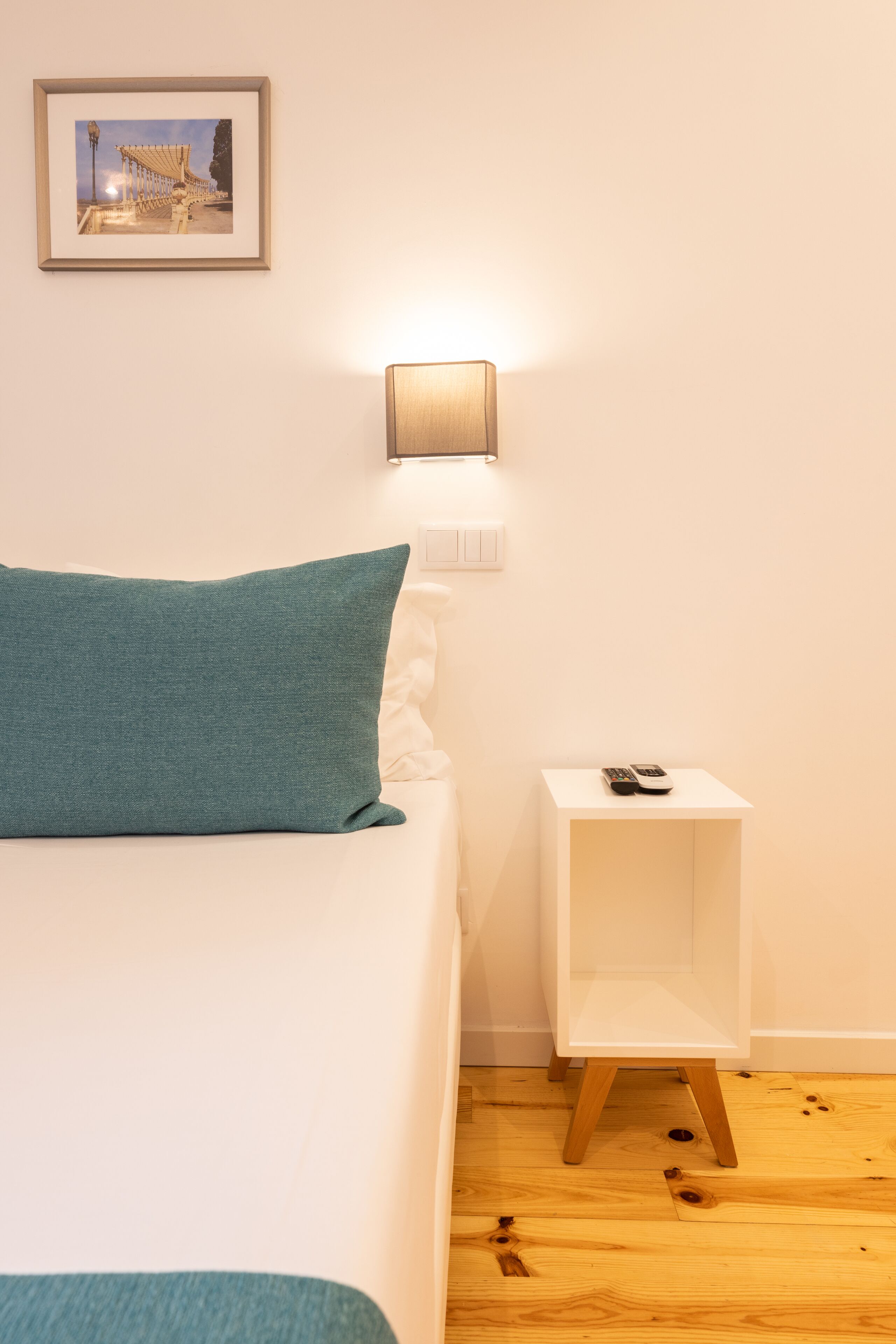 A neatly arranged bedroom with a bed, a bedside table with a lamp, and a small shelf.