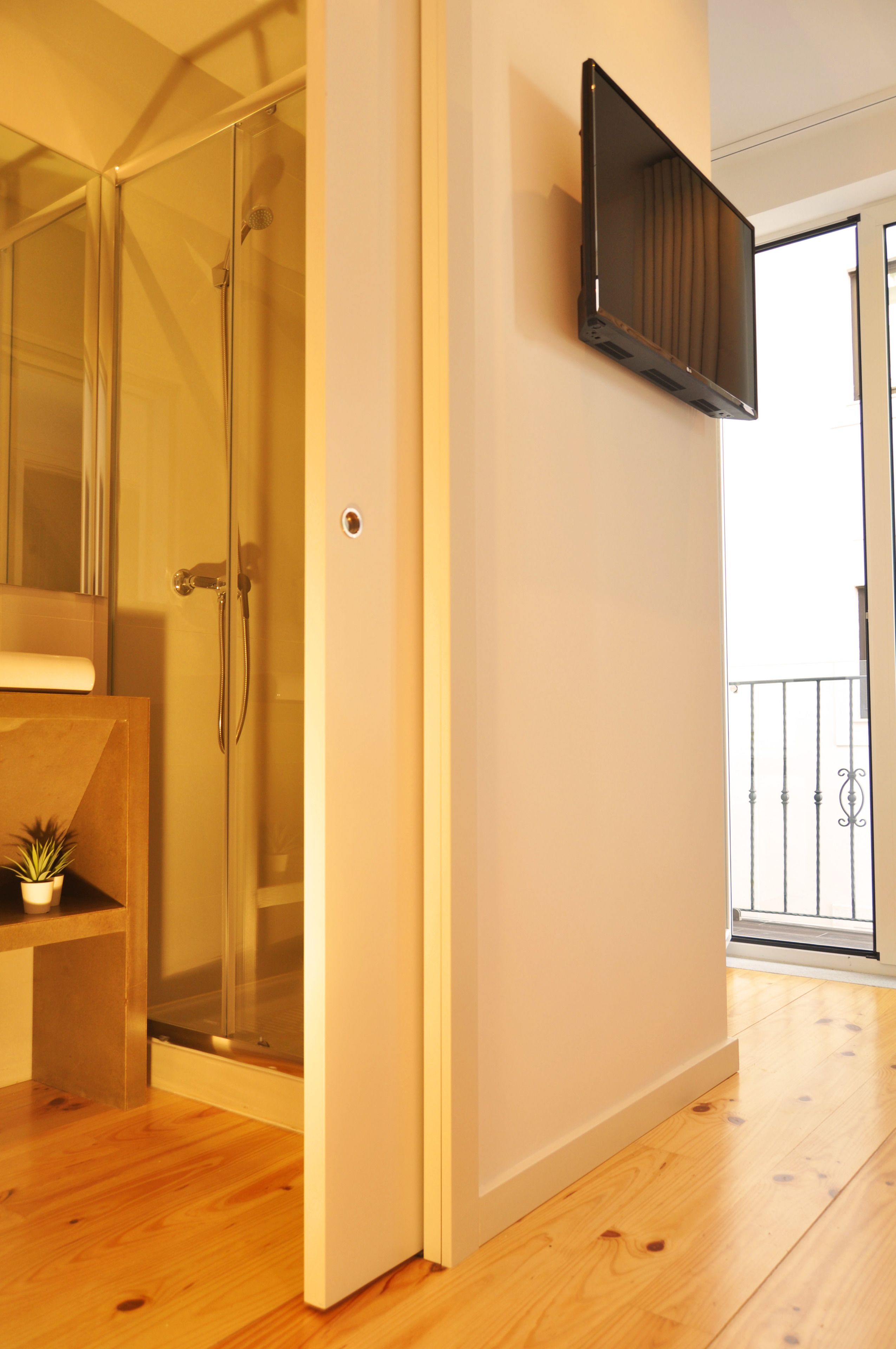 A modern bathroom with a glass shower enclosure, a mounted television, and a wooden floor.