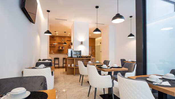 Un café moderno con mesas, sillas, una zona de cocina e iluminación colgante.