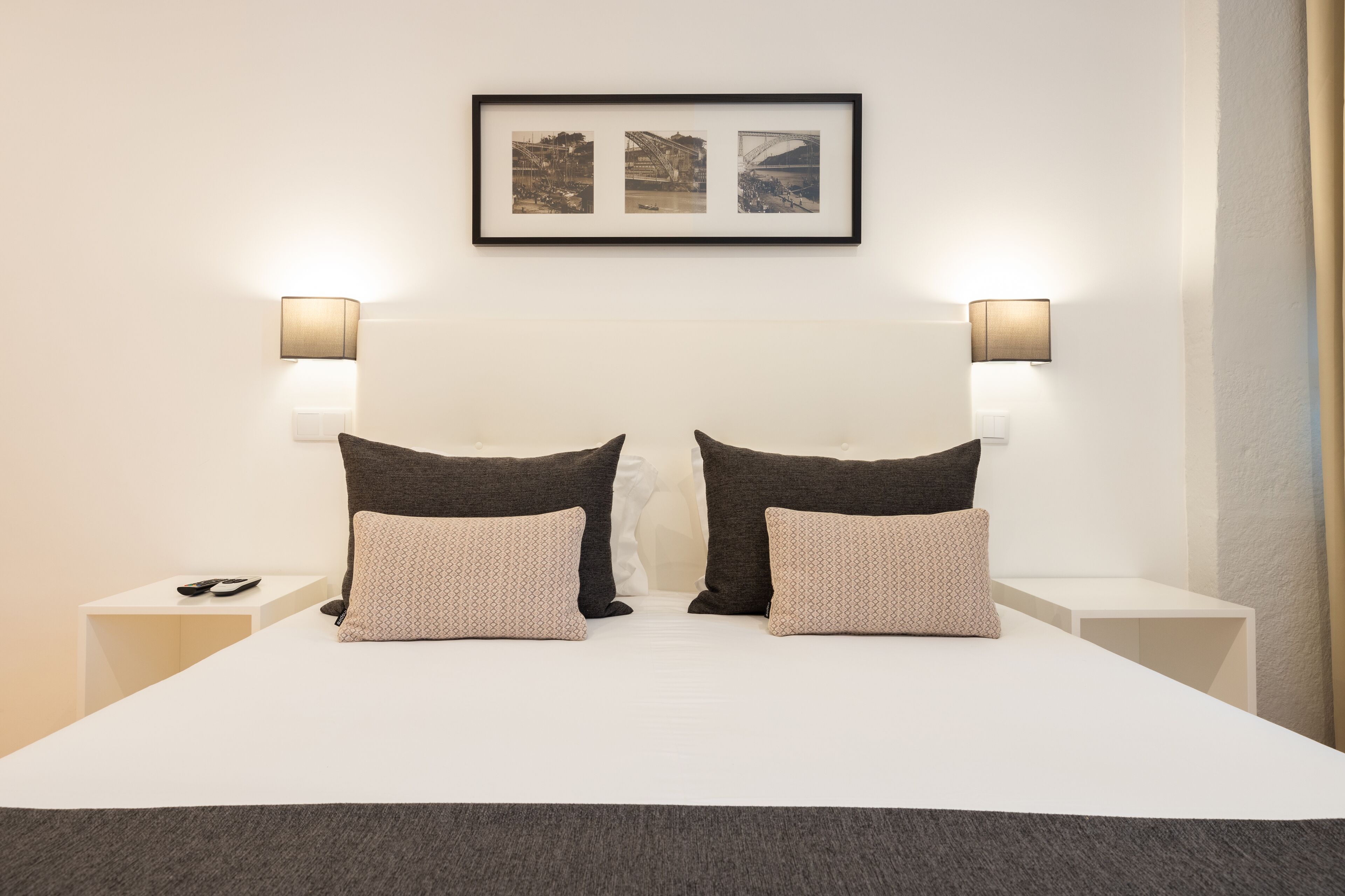 A neatly made bed with two pillows, a framed picture above, and two bedside lamps.