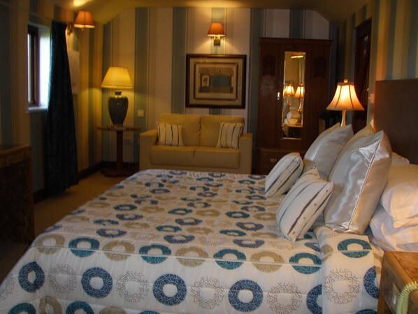 A hotel room with a large bed, a sofa, a lamp, and a mirror. - Cornfields Hotel & Restaurant (Bedford)