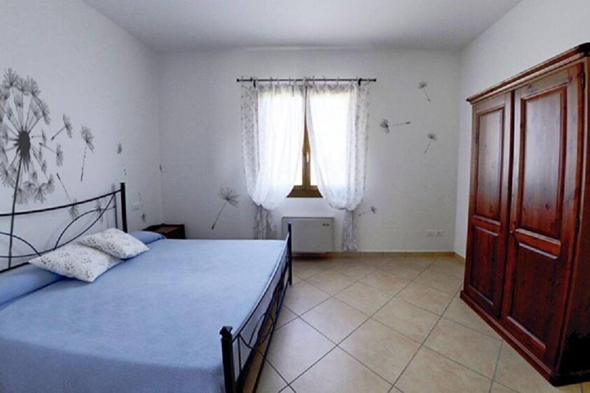 Een slaapkamer met een bed, een kast, een radiator en een raam met gordijnen.