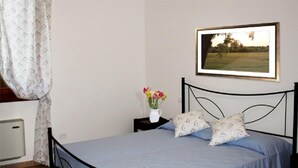 A bedroom with a bed, a nightstand, a framed picture, and a window with curtains. - Agriturismo Cà Pisani (Porto Viro)