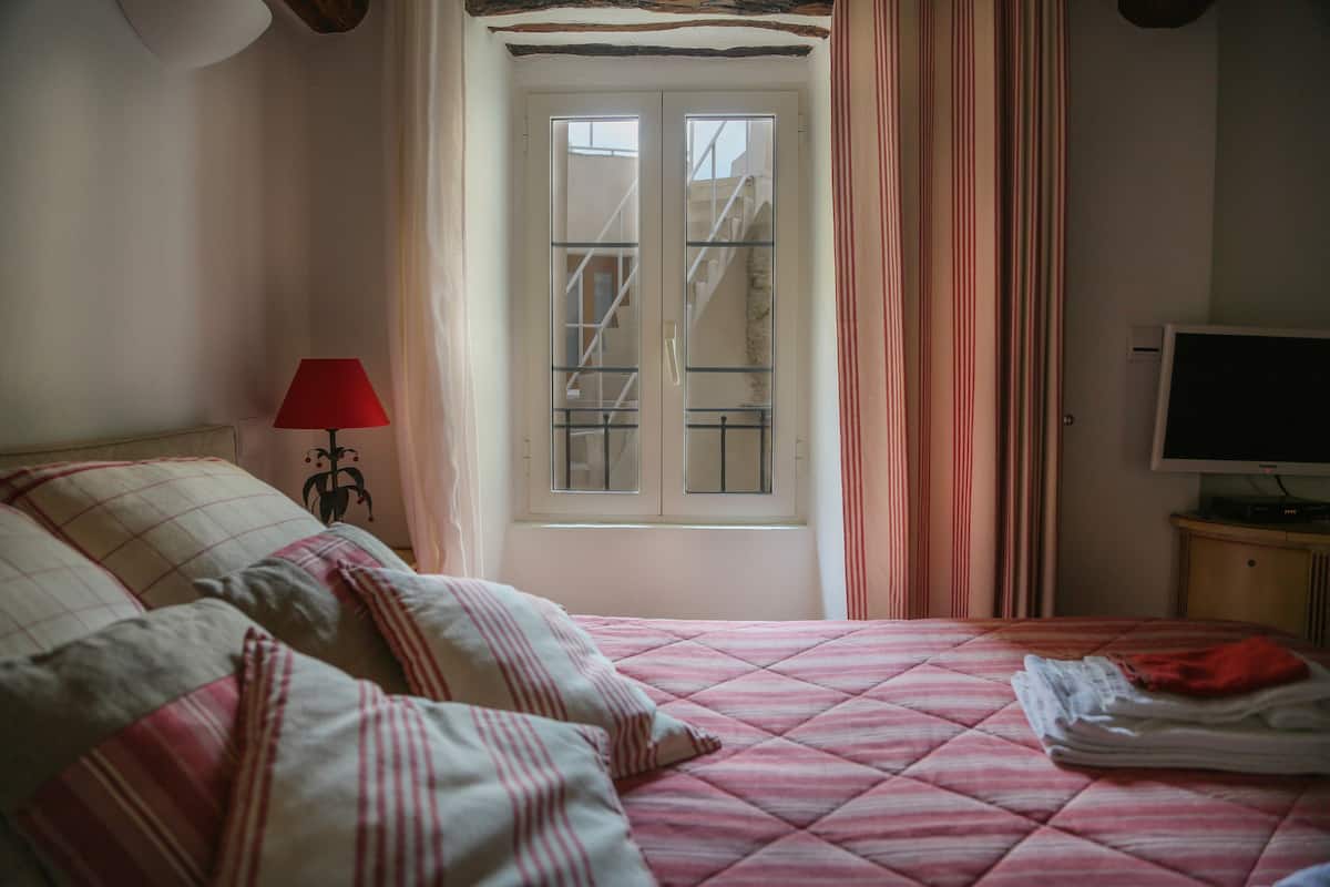 Een slaapkamer met een bed, een rode lamp, een televisie en een raam met gordijnen.