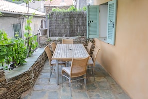 Un patio con pavimento in pietra, un tavolo di legno e sedie in vimini, circondato da un muro in pietra e un recinto verde.