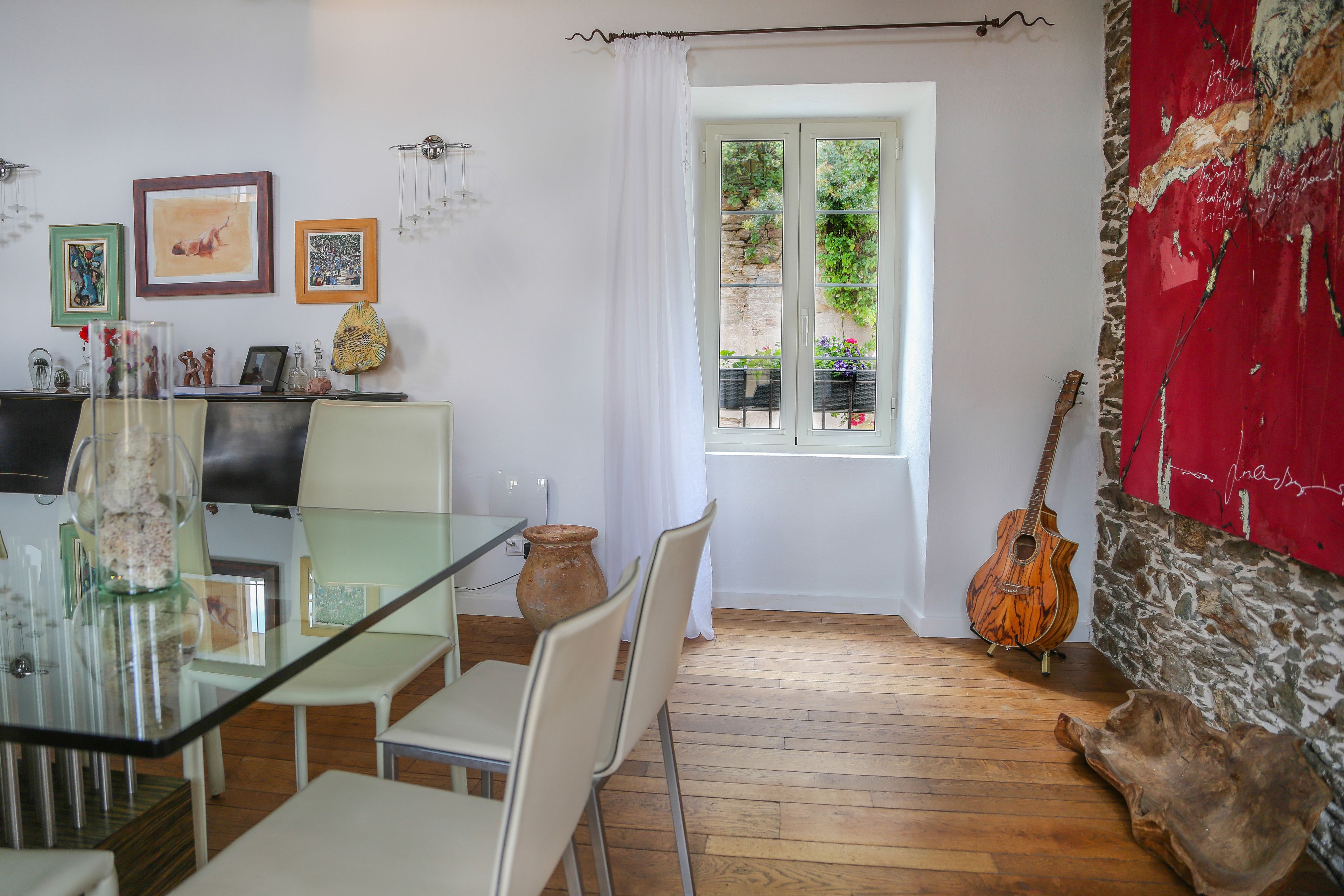 A dining area with a glass table, white chairs, a wooden guitar, and a stone wall.