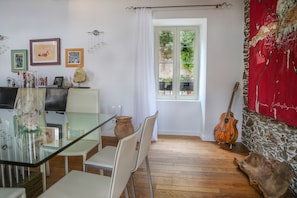 Zona pranzo con tavolo in vetro, sedie bianche, una chitarra di legno e un muro in pietra.