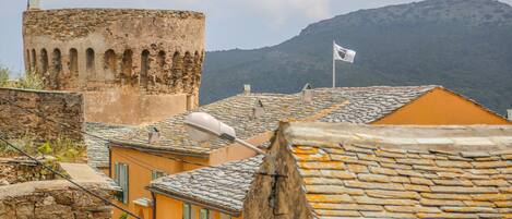 Una torre de piedra histórica con ventanas de arco, una bandera y techos de tejas tradicionales.