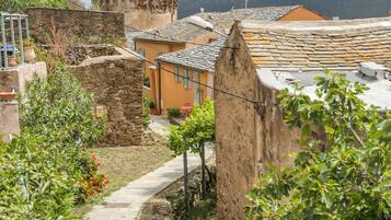 A stone pathway leading through a rustic village with traditional stone buildings and a tower in the background.