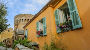 Une rue étroite bordée d’un immeuble aux volets verts et aux jardinières fleuries.