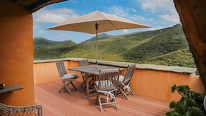 Une terrasse en bois avec une table et des chaises, un parasol et une vue sur des collines verdoyantes.